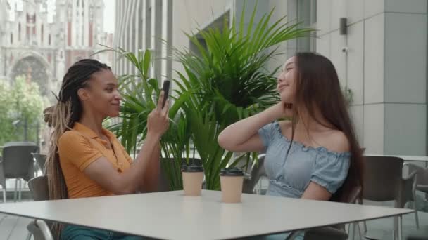 Радісні молоді жінки роблять фото позування на камеру смартфона в сучасному кафе — стокове відео