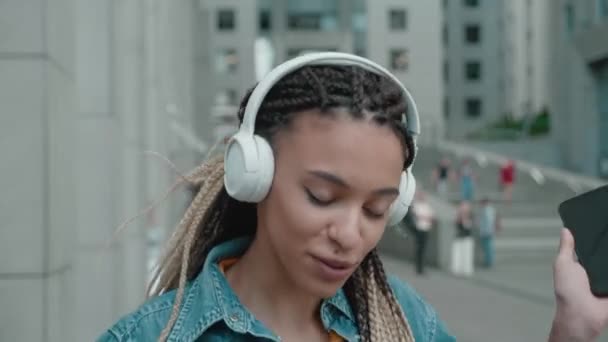 Retrato de mujer joven atractiva de raza mixta moderna con auriculares al aire libre — Vídeos de Stock