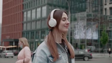 Kablosuz kulaklıklı mutlu beyaz kız şehir sokaklarında akıllı telefon ve dans kullanarak müzikten zevk alıyor. Gençlik ve yaşam tarzı kavramı.
