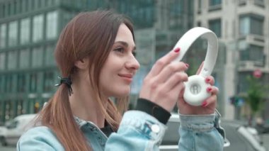 Gülümseyen kadın kulaklıklarını takıyor ve dışarıda müzik dinliyor..