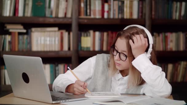 Chica adolescente cansada, mujer joven escuela usar auriculares con gafas aprender a ver webinar en línea clase webcast mirando elearning portátil haciendo notas o videollamadas profesor remoto. — Vídeos de Stock