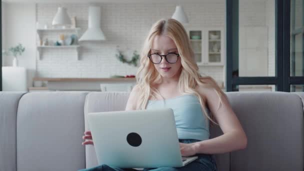Blond žena s brýlemi sedí na gauči a psaní na notebooku po tomto zavřel notebook a sedí na gauči se smyslem pro dokončenou práci — Stock video
