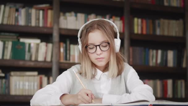 Kulaklık takan mutlu liseli kız öğrenci sanal ders sınıfında el mesafesini yükselterek bilgisayar öğretmeniyle kütüphanede video konferans görüşmeleri yaparak öğreniyor. — Stok video