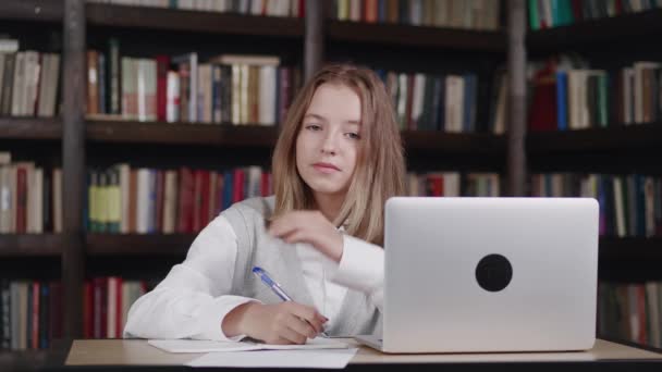 Sonriente alumna preadolescente inteligente estudiando en casa sentada en el escritorio. Feliz niño lindo estudiante de primaria escribiendo en el libro de ejercicios haciendo la tarea, aprendiendo en la mesa. — Vídeos de Stock