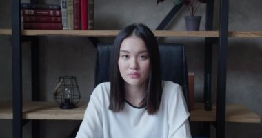 Çekici genç Asyalı kadın model kameraya bakıyor, mutlu 20 'li yaşlarda esmer kadın profesyonel kısa saçlı, yalnız oturan modern çatı katı ofisi, yakın plan portresi.