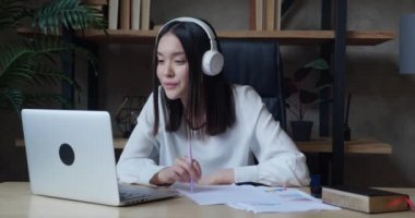 Kablosuz kulaklık takan, internetten ders çalışan, kağıt notlar kullanan Asyalı bir öğrenci. Motivasyonlu milenyum internet öğretmeni konferans video çağrısına göre dil dersi veriyor.