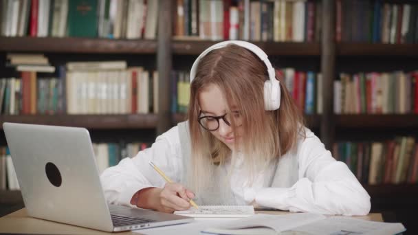 Vit tonåring flicka, ung kvinna skola bära hörlurar lära sig att titta på online webinar webcast klass tittar på bärbar dator elärande att göra anteckningar eller videosamtal avlägsen lärare. — Stockvideo