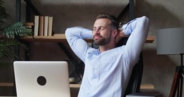 Gülümseyen ve memnun iş adamı iyi iş çıkardığı için seviniyor, ve başarılı bir günün ardından dinleniyor, sandalyeye yaslanıyor ve gülümsüyor, erkek çalışan projesini bitirdi