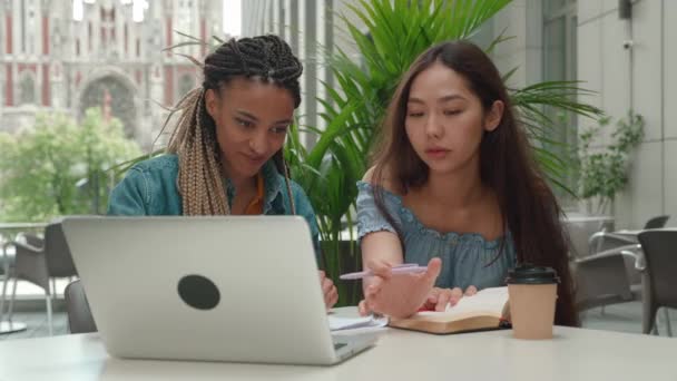 Estudantes multirraciais estudam juntos preparam projeto olhando tela laptop, fazer anotações, equipe de jovens escrever resumo ensaio aprender em trabalho de equipe fazer pesquisa criativa lição de casa em uma cafeteria — Vídeo de Stock