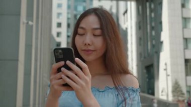 Akıllı telefona bakan çekici Asyalı kadın piyangoda kazanmak için heyecanlı çok mutlu ve açık havada gülümsüyor. Modern teknoloji konseptinde iyi haber mesajı