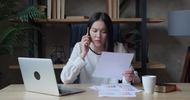 Азиатская бизнесвумен, использующая ноутбук и звонящая на смартфон, одновременно работает сверхурочно в офисе бизнес-стартапа. Занятый многозадачный занятой сотрудник, анализирующий финансовую статистику переутомительного написания — стоковое видео