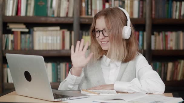 Aluno inteligente adolescente menina escola usar fones de ouvido aprender on-line com professor tutor mão acenando usando videoconferência chamada pela webcam no computador portátil. Educação em videoconferência. — Vídeo de Stock