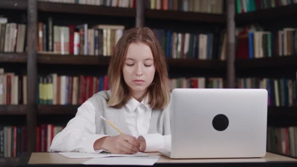 Uśmiechnięta nastolatka ucząca się w domu, siedząca za biurkiem. Szczęśliwy słodkie dziecko uczennica szkoły podstawowej pisanie w zeszyt ćwiczeń robi pracę domową, nauka przy stole. — Wideo stockowe