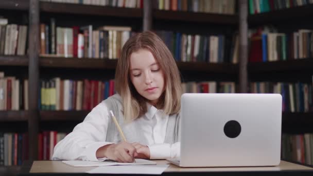 Zbliżenie portret uczennica uczyć lekcji podczas gdy w domu siedzi przy stole w bibliotece za pomocą laptopa, książki, notebook. — Wideo stockowe