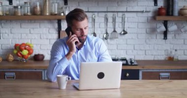 İş adamı dizüstü bilgisayara bakıyor ve evde telefonla konuşuyor. İş adamı cep telefonunu ara