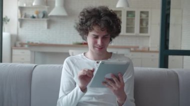 Dijital tablet şirket yazılımını kullanan genç profesyonel bir işçi koltukta oturuyor, gülümseyen bir erkek yönetici evdeki ped bilgisayar teknisyeninde çalışıyor.