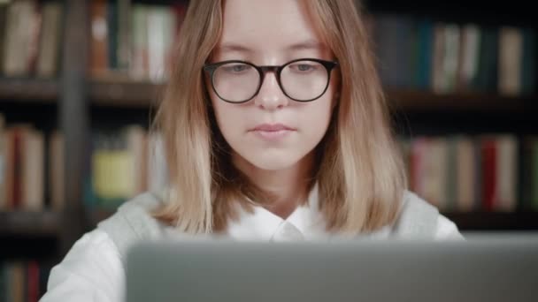 Stanco giovane studentessa, sta lavorando sul computer portatile alla scrivania in una stanza accogliente sullo sfondo della biblioteca. Girlis ha esaurito la testa sfregante e guardando lo schermo e sbadigliare. Concetto di studio a distanza — Video Stock