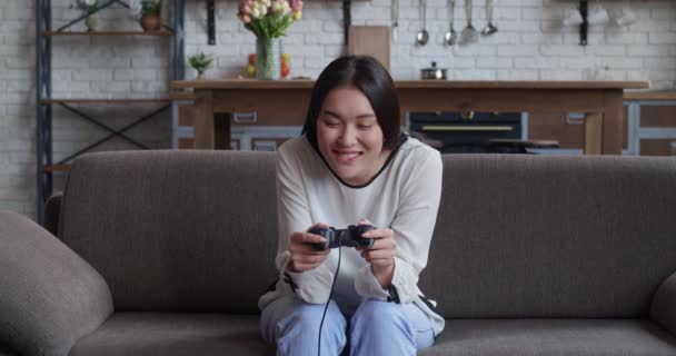 Energieke jonge Aziatische vrouw met behulp van jostick draadloze gamepad controllr het spelen van moderne video games op de console. Blijf thuis. Amusement. — Stockvideo