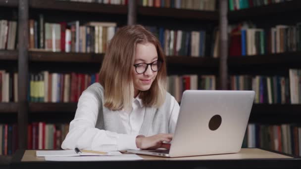 Chica con el pelo corto con gafas trabajando en la biblioteca de la escuela. Usa la computadora.. — Vídeos de Stock