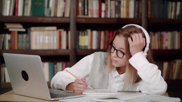 Enfocado mujer joven escuela usar auriculares con gafas aprender a ver webinar en línea webcast clase mirando elearning portátil haciendo notas o videollamadas profesor remoto. — Vídeo de stock
