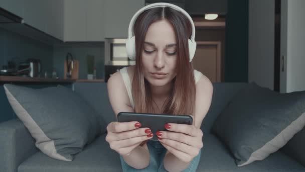 Žena se sluchátky sedí s hraje smartphone. Žena hraje online hru na internetu smartphone. Mladá dívka je poražen v online hře. — Stock video