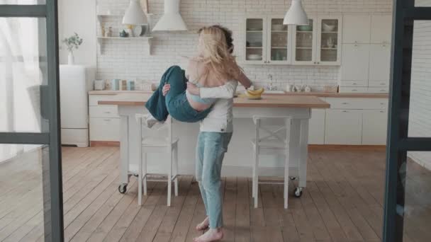 Una pareja feliz dando vueltas en una casa nueva. Pareja joven celebrando la reubicación juntos. Hombre y mujer sonrientes divirtiéndose en una casa de lujo. Amor pareja abrazándose en nuevo apartamento — Vídeo de stock