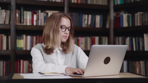 Távoktatási koncepció. Serdülő iskoláslány szemüvegben tanul online laptoppal jegyzetel a másolókönyvben. Tini lány iskolás hallgató visel fejhallgató néz internetes videó tanfolyam ül a — Stock videók