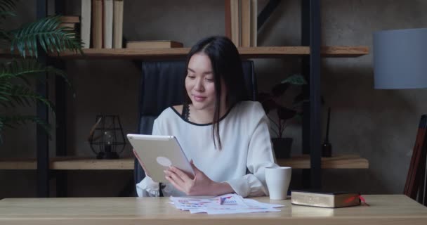 Zakelijke vrouw zit achter bureau in kantoor met behulp van tablet. Jonge ondernemer lacht, surft op internet of werkt — Stockvideo