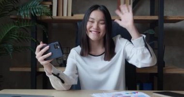 Modern ofisteki bir kadın cep telefonuyla görüntülü konuşma yapıyor. Video konferans video kaydı üzerinden konuşuyorum. Uzaktan haberleşme.