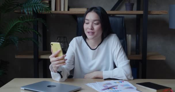 Ung asiatisk kvinna gör videosamtal chatta online på mobiltelefon i moderna kontor. Talar över video samtal konferens inspelning vlog. Fjärrkommunikation på distans. — Stockvideo