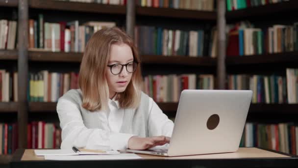 Дівчина використовує ноутбук, вводячи текст, що дивиться дистанцію онлайн-навчання семінар клас, віддалений вебінар або віртуальну зустріч класу в університетському бібліотечному просторі . — стокове відео