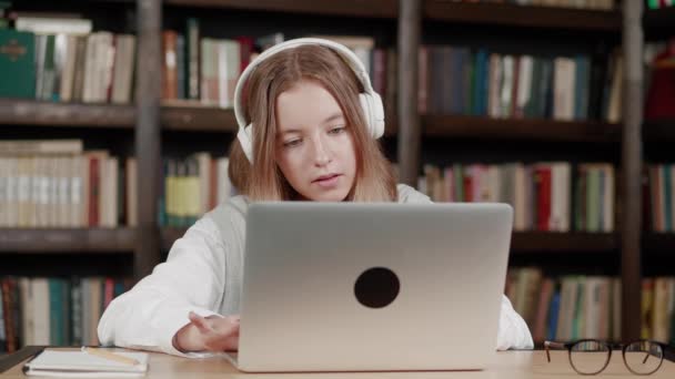 La ragazza fa le lezioni, i compiti sul computer portatile in biblioteca moderna la formazione remota. quarantena ed epidemia. — Video Stock