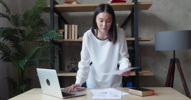 Joven mujer de negocios asiática que trabaja con el ordenador portátil y los papeles, mujer ocupada pagando facturas de banca en línea, hacer cambios para informar, la gestión de las finanzas de verificación de presupuesto haciendo papeleo utilizando la computadora femenina — Vídeos de Stock