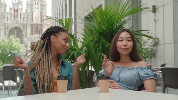 アジアの女性に結婚の輪を示す混合人種の女性。友人はニュースに嫉妬してる。屋外のカフェに座っている2人の友人 — ストック動画