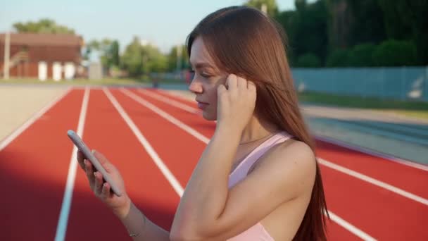 Attraktiv sporttjej med fitness tracker och kör app bärbar teknik med smartphone och hörlurar. En hälsosam livsstil. — Stockvideo