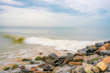 Okyanus sakin ve kayalar kıyı boyunca dağılmış. Gökyüzü bulutlu ve su açık mavi bir renk.