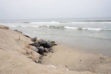 Arka planda büyük bir su kütlesi olan kayalık bir sahil. Kumsal kayalar ve molozlarla kaplı ve su dalgalı. Manzara kasvetli ve ıssız, kayalarla birlikte.