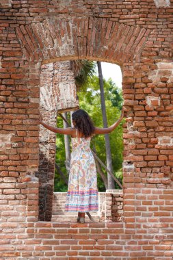 Bir kadın tuğla bir duvarın önünde duruyor, pencereden dışarı bakıyor. Tuğla duvar eski ve yıpranmış, ve kadının elbisesi renkli ve akıcı. Bu sahnede nostalji ve özlem duygusu var.