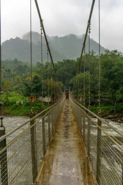 Arka planda sisli bir gökyüzü olan bir nehir üzerinde köprü. Köprü metalden yapılmıştır.
