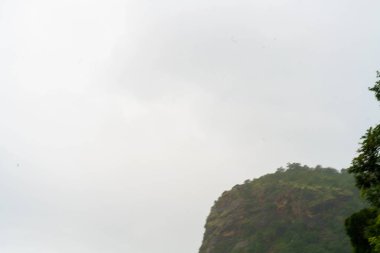 Arkasında bulutlu bir gökyüzü olan dağ. Gökyüzü gri ve dağ ağaçlarla kaplı.