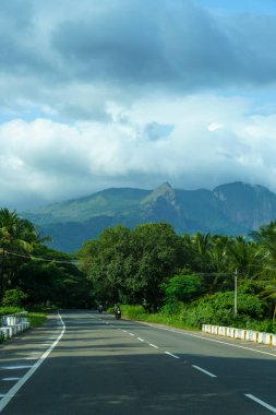 Arka planda dağ olan bir yol. Yol boş ve gökyüzü bulutlu.