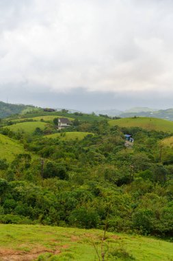 Uzakta evi olan yemyeşil bir yamaç. Gökyüzü bulutlu.