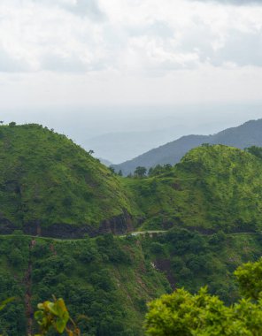 Dağlar yemyeşil ağaçlarla kaplı ve gökyüzü bulutlu. Huzur dolu bir sahne.
