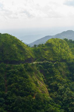 Dağlar yemyeşil ve yemyeşil, tepelerin arasından geçen dolambaçlı bir yol var.