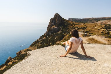 Kız bir rock ve denize bakarak oturur