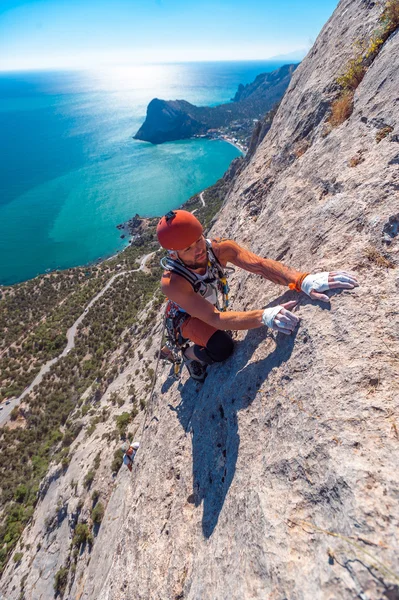 The climber climbs the rock against the sea — Stock Photo, Image