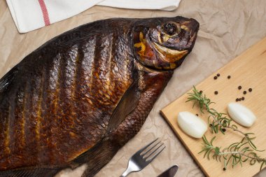 Tütsülenmiş balık çamı masanın üzerinde bir peçete, çatal, bıçak, soğan ile ahşap bir tahtanın üzerinde yatıyor.