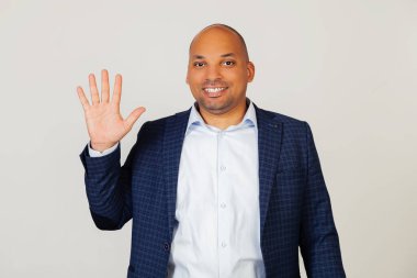Beş numaralı parmaklarıyla gülümseyen, kendinden emin ve mutlu genç Afrikalı Amerikalı iş adamının portresi. Adam beş parmak gösteriyor. 5 numara. Gri bir arka planda duruyor.