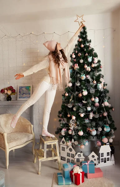 Mutlu genç kadın Noel ağacını süslüyor. Süveter giyen bir kız Noel ağacının tepesine yıldız koyar. Yeni yıl ve Noel tatili konsepti
