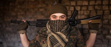 Elinde silahlarla milli keffiyeh 'den başlıklı Arap erkek asker. Tuğla duvarın arkasında ateşli silahları olan bir Müslüman.